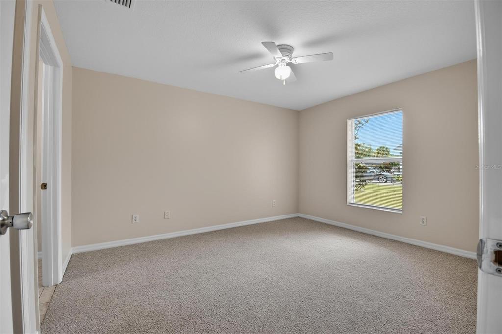 An empty bedroom with beige walls, tan carpeting, a ceiling fan, and a single window — 83 LYNBROOK DRIVE UNIT A, PALM COAST, FL