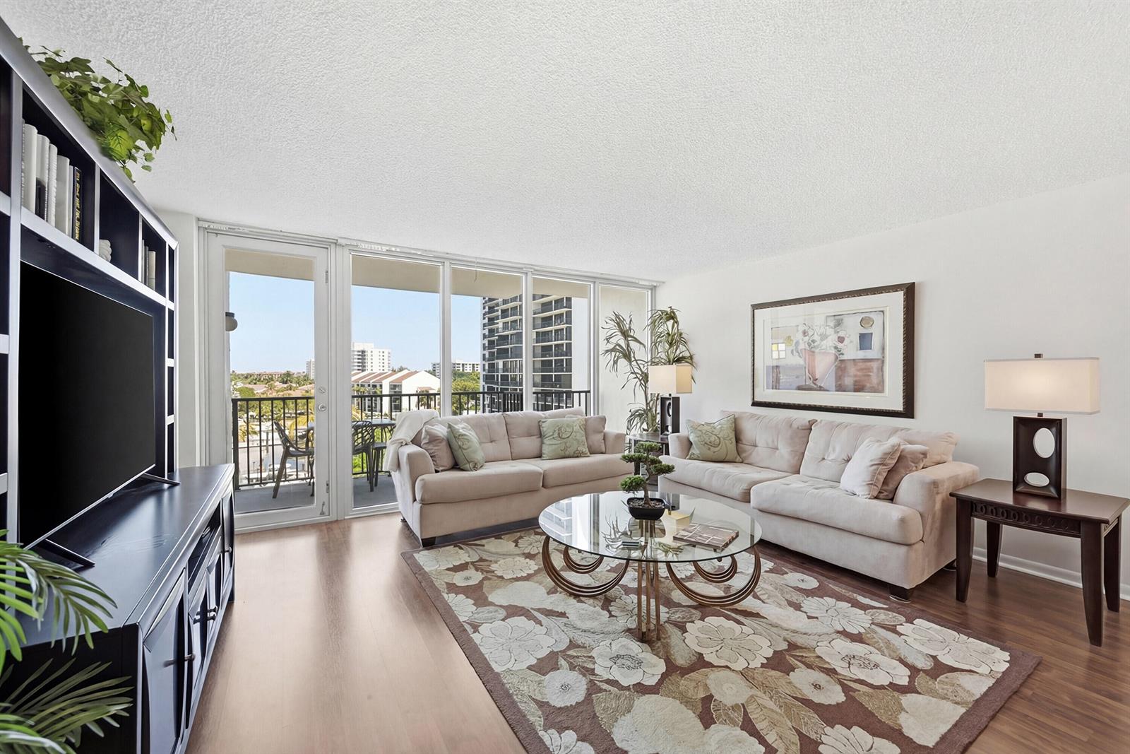 A living room features beige sofas, a glass coffee table, and a balcony with city views — 4750 S Ocean Boulevard # 512, Highland Beach FL 33487, HIGHLAND BEACH, FL
