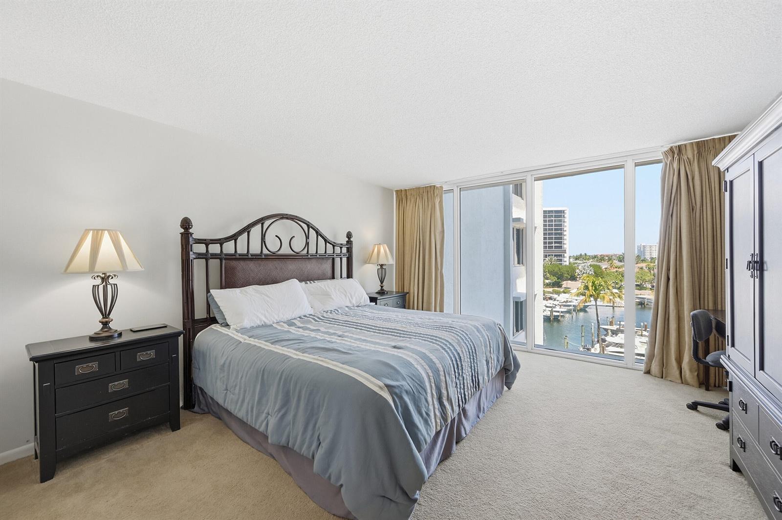 A bedroom features a bed, dark furniture, and floor-to-ceiling windows overlooking a marina — 4750 S Ocean Boulevard # 512, Highland Beach FL 33487, HIGHLAND BEACH, FL