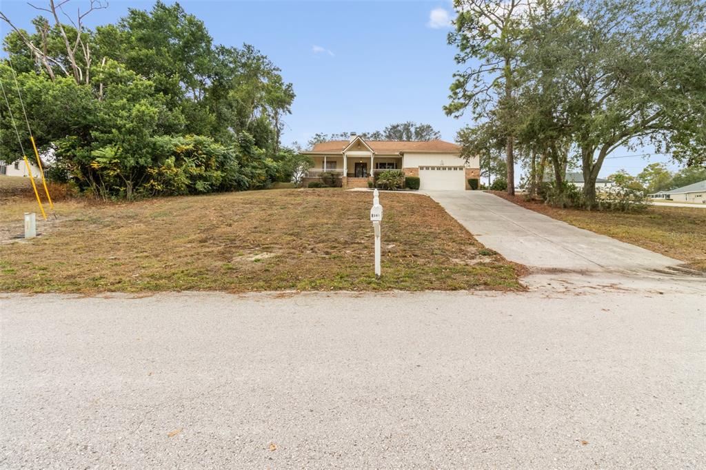 A single-story house with a tan exterior, a front porch, and a concrete driveway — 5301 MERRIFIELD COURT, SPRING HILL, FL