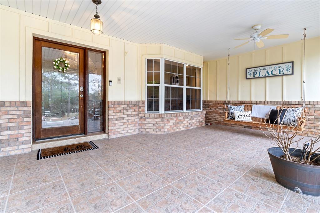 A covered front porch features tiled flooring, a brick base, a wooden swing, and a door — 5301 MERRIFIELD COURT, SPRING HILL, FL