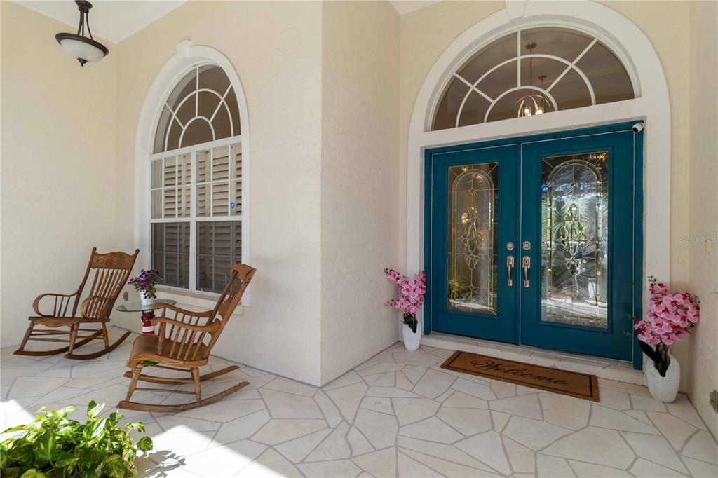 A covered front porch features two wooden rocking chairs, a teal double door, and tile flooring — 1860 CITRON STREET, PORT CHARLOTTE, FL