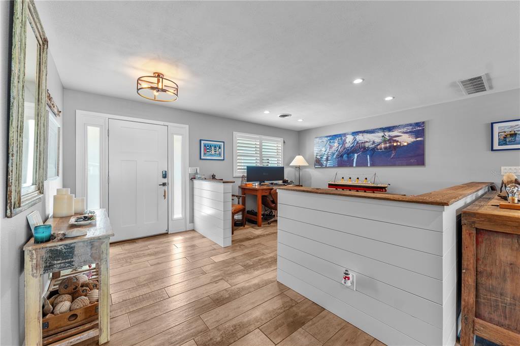 An entryway with wood-look tile floors leads to a home office behind a shiplap half-wall — 118 CORAL WAY, PORT ORANGE, FL