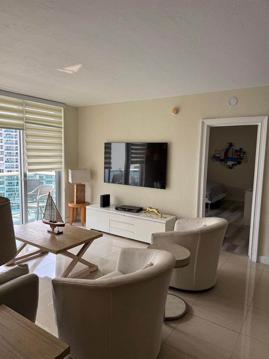 A living room features tile floors, a wall-mounted television, and two beige armchairs — 3801 S Ocean Dr # 14V, Hollywood FL 33019, HOLLYWOOD, FL