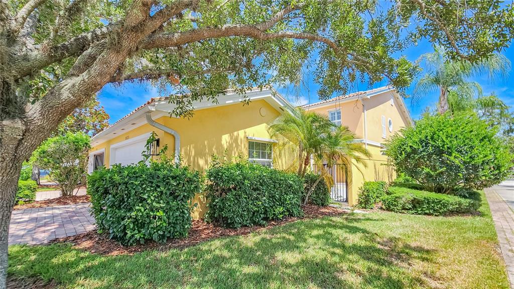 A yellow two-story house with a garage, landscaping, and a paved driveway under large trees — 8523 LEATHERLEAF LANE, ORLANDO, FL