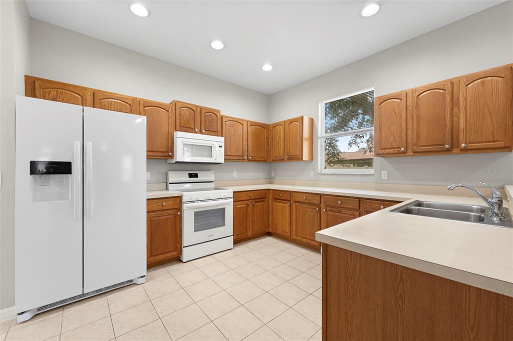 A kitchen features oak cabinets, white appliances, beige countertops, and light-colored tile flooring — 10215 CYPRESS KNEE CIRCLE, ORLANDO, FL
