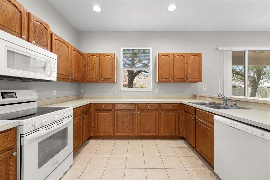 A kitchen with wood cabinets, beige countertops, and tile flooring opens to a living area — 10215 CYPRESS KNEE CIRCLE, ORLANDO, FL