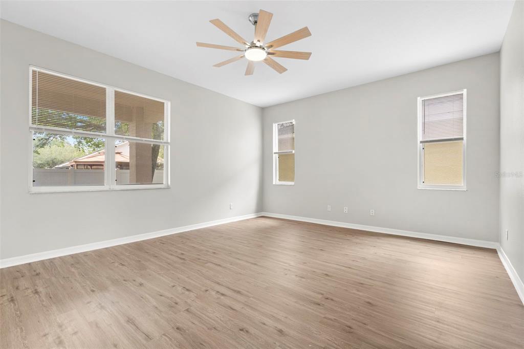 An empty room with light wood-look flooring, gray walls, a ceiling fan, and three windows — 10215 CYPRESS KNEE CIRCLE, ORLANDO, FL