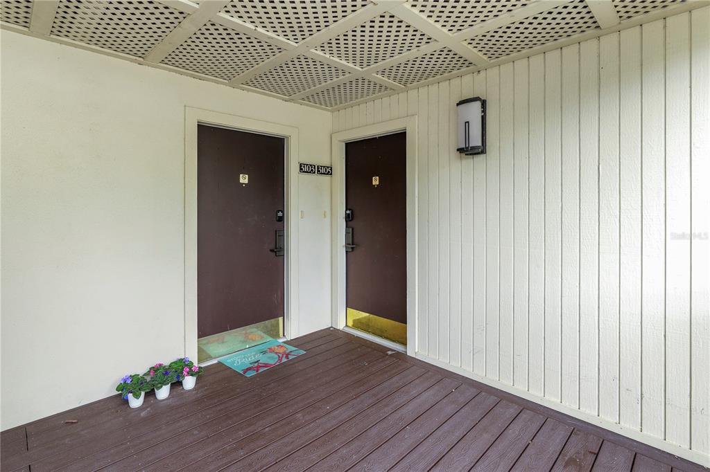 A covered wooden deck features two brown apartment doors with unit numbers above them — 4947 MILL POND ROAD UNIT 3103, WESLEY CHAPEL, FL