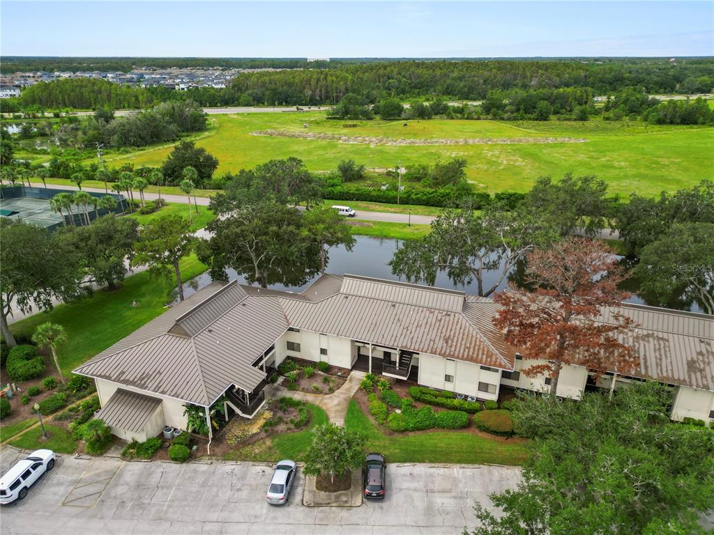 An aerial view shows a multi-unit building with a metal roof beside a pond — 4947 MILL POND ROAD UNIT 3103, WESLEY CHAPEL, FL