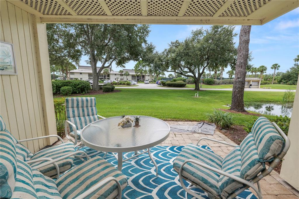 A covered patio features a glass-topped table and striped chairs overlooking a grassy lawn — 4947 MILL POND ROAD UNIT 3103, WESLEY CHAPEL, FL