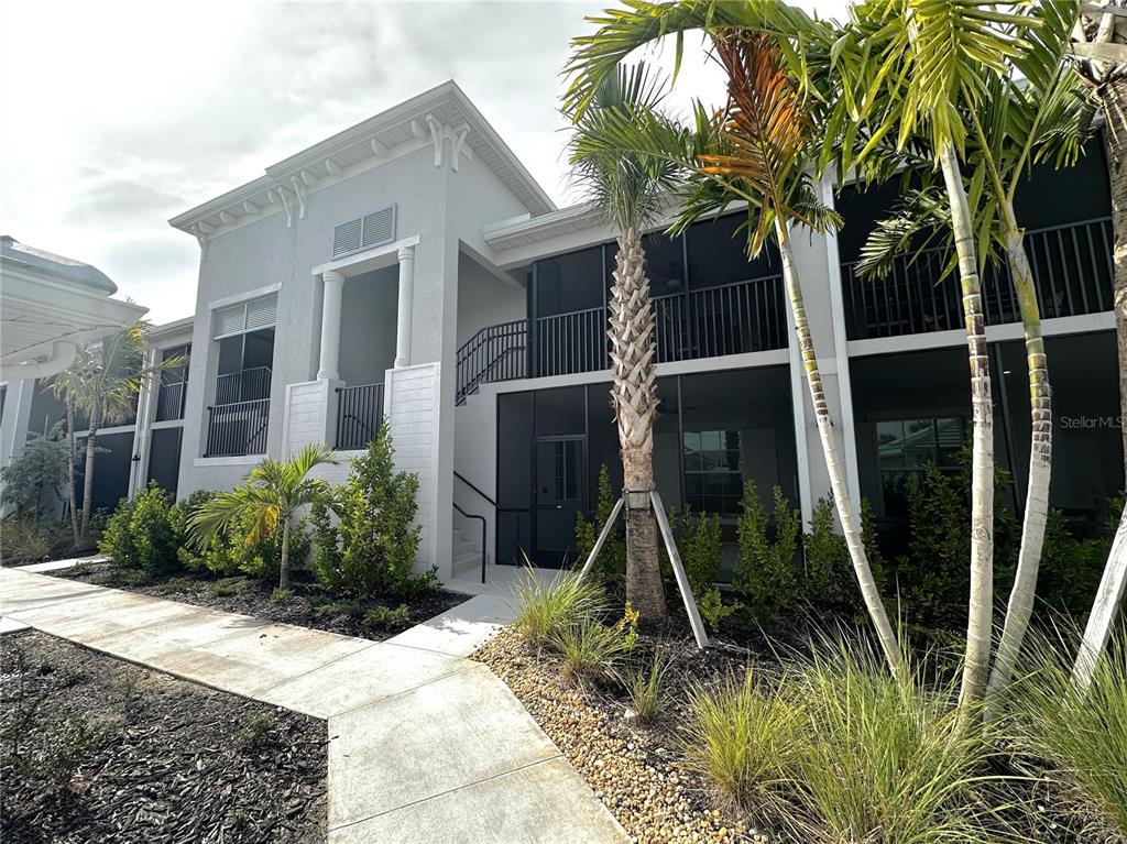 The exterior of a two-story building features a screened-in balcony and a concrete walkway — 14221 HERITAGE LANDING BOULEVARD UNIT 2024, PUNTA GORDA, FL