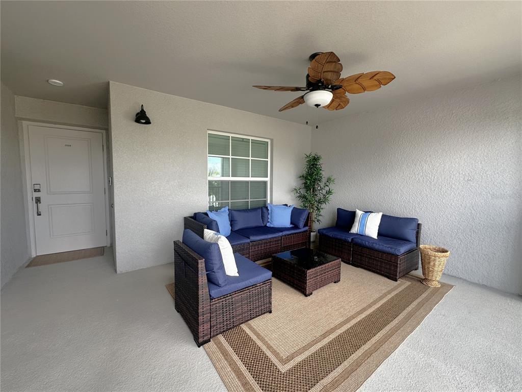 A covered patio features wicker furniture with blue cushions, a ceiling fan, and a rug — 14221 HERITAGE LANDING BOULEVARD UNIT 2024, PUNTA GORDA, FL