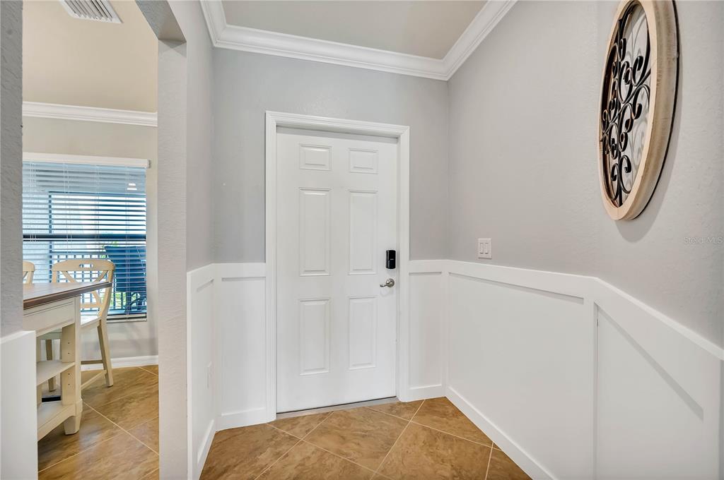 An entryway features a white door, wainscoting, and tile flooring with a view into a dining area — 5577 PALMER CIRCLE UNIT 201, BRADENTON, FL
