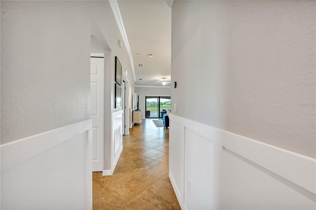 A hallway with white wainscoting and tile flooring leads toward a living area with views — 5577 PALMER CIRCLE UNIT 201, BRADENTON, FL