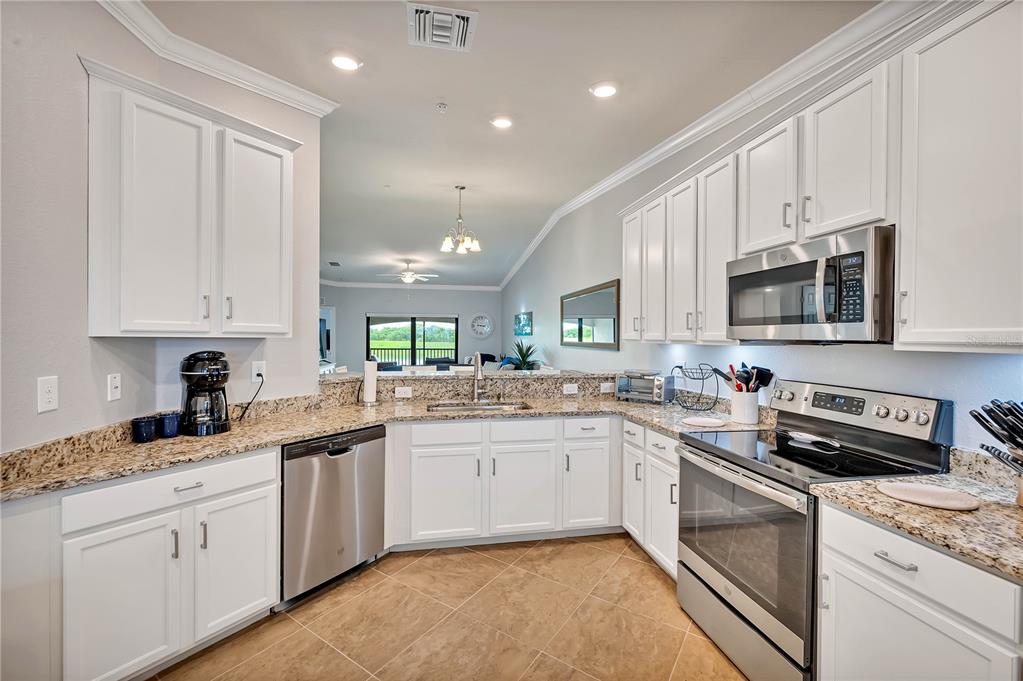 A kitchen with white cabinets, granite countertops, stainless steel appliances, and tile flooring — 5577 PALMER CIRCLE UNIT 201, BRADENTON, FL
