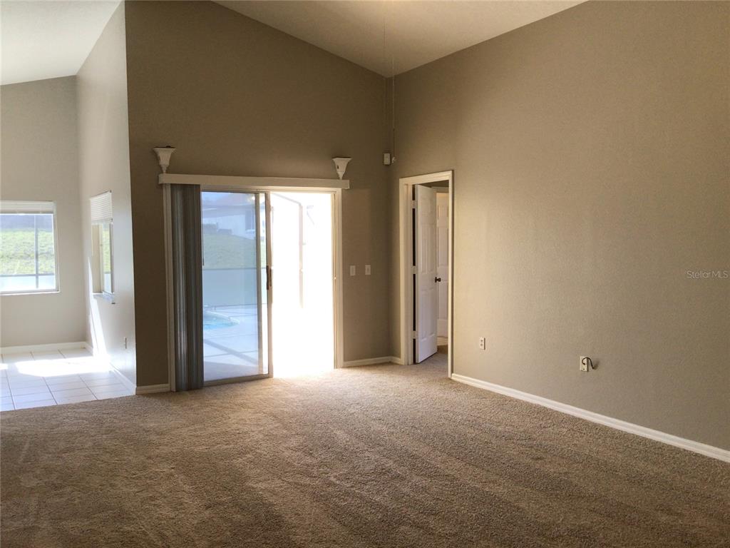 A carpeted living room features vaulted ceilings, a sliding glass door, and a doorway — 509 HILLCREST DRIVE, DAVENPORT, FL