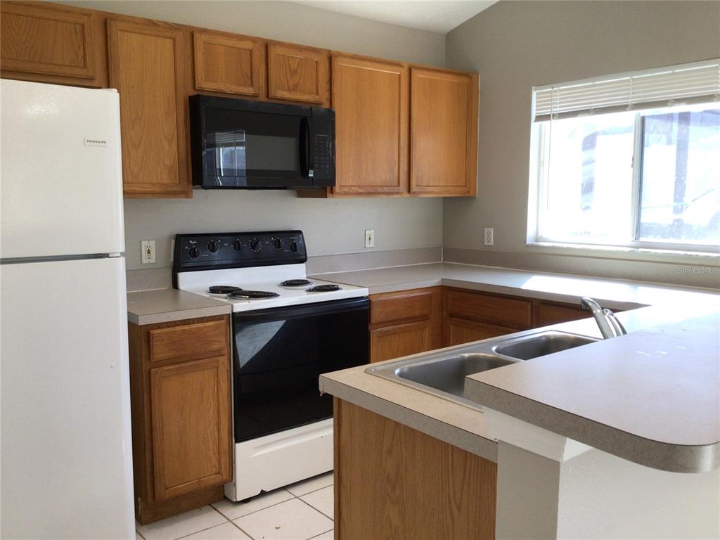 A kitchen features wood cabinets, white appliances, laminate countertops, and a double-basin sink — 509 HILLCREST DRIVE, DAVENPORT, FL