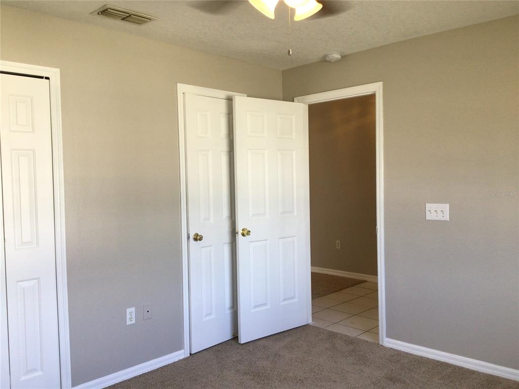 A bedroom features beige walls, carpeted flooring, white closet doors, and an open doorway — 509 HILLCREST DRIVE, DAVENPORT, FL