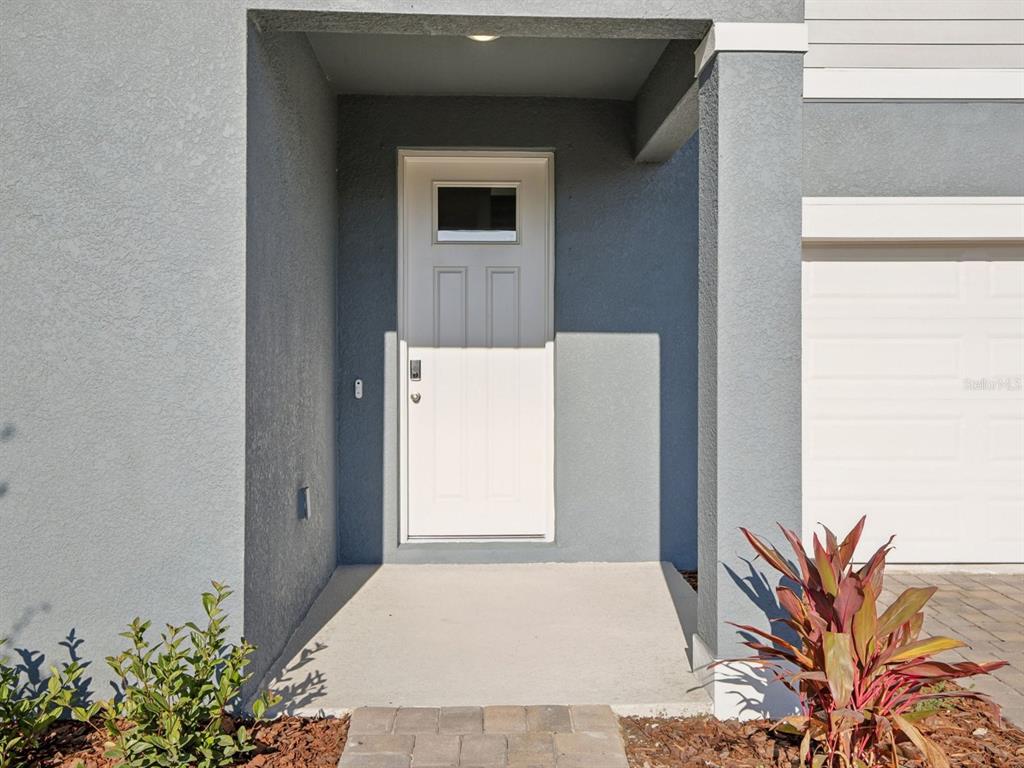 A white front door is recessed under a covered entryway next to a garage — 13311 SHELLMORE AVENUE, PALMETTO, FL