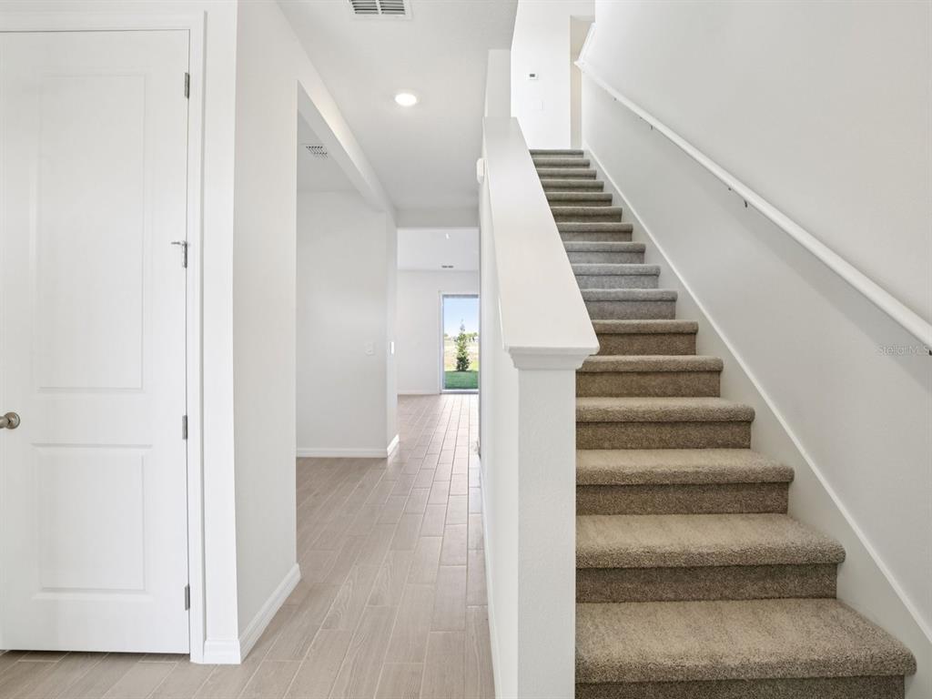 A hallway with light wood-look tile flooring leads to a staircase with beige carpet — 13311 SHELLMORE AVENUE, PALMETTO, FL