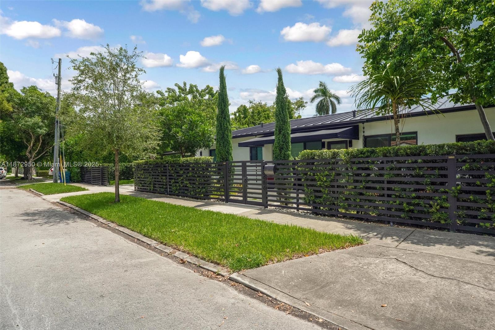 A single-story house with a dark metal roof is enclosed by a horizontal slat fence — 2484 SW 25th St, Miami FL 33133, MIAMI, FL