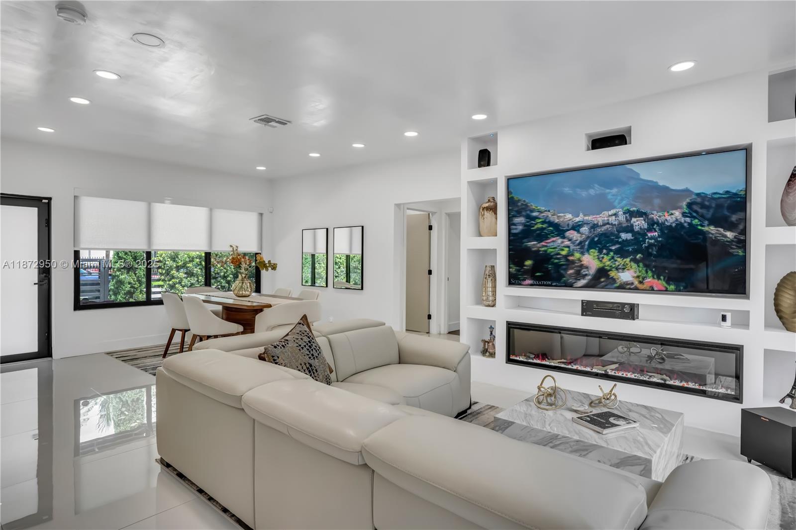 A modern living room features a white sectional sofa, a fireplace, and a large television — 2484 SW 25th St, Miami FL 33133, MIAMI, FL