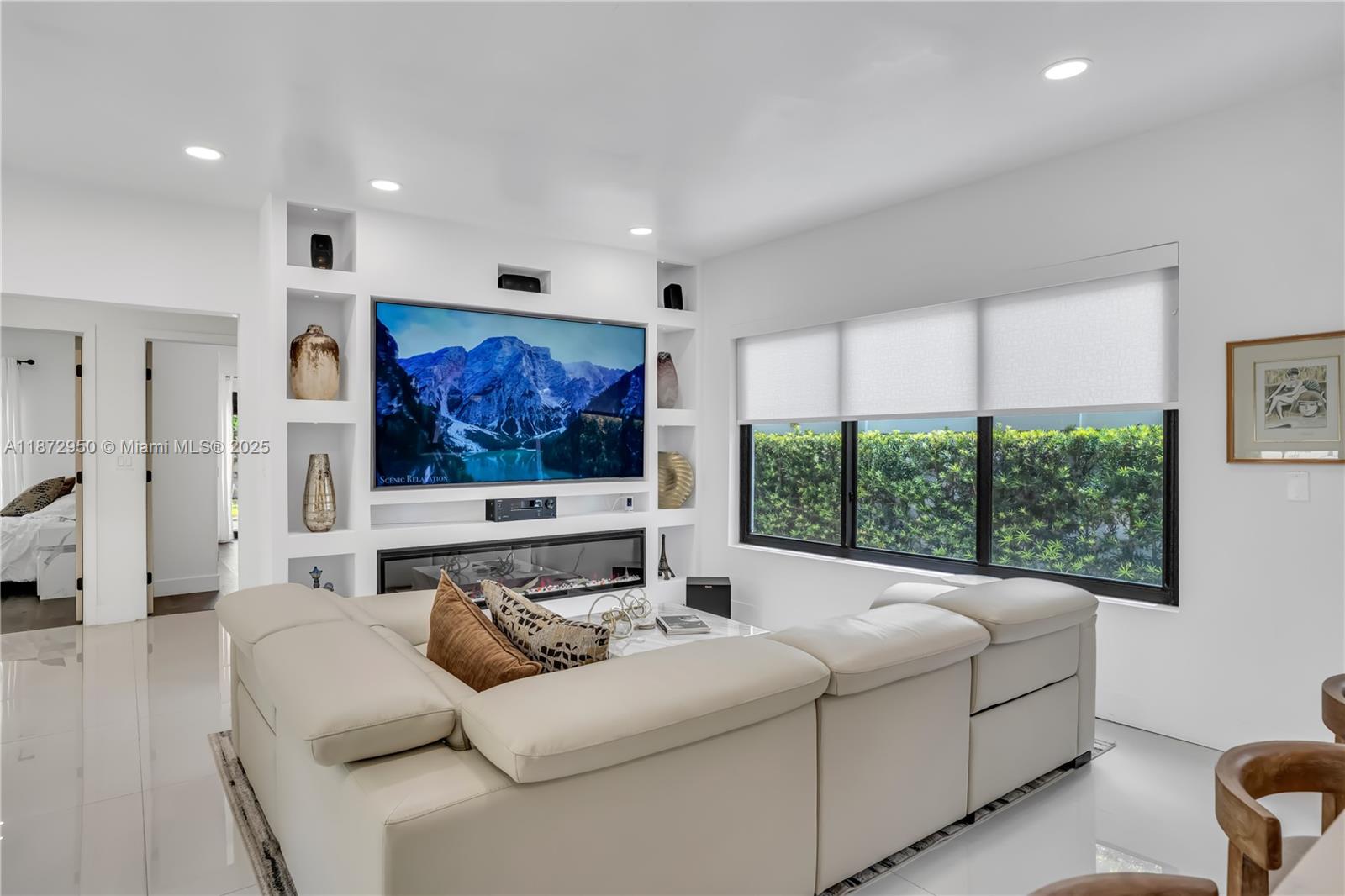 A modern living room features a large sectional sofa, a built-in media wall, and a fireplace — 2484 SW 25th St, Miami FL 33133, MIAMI, FL