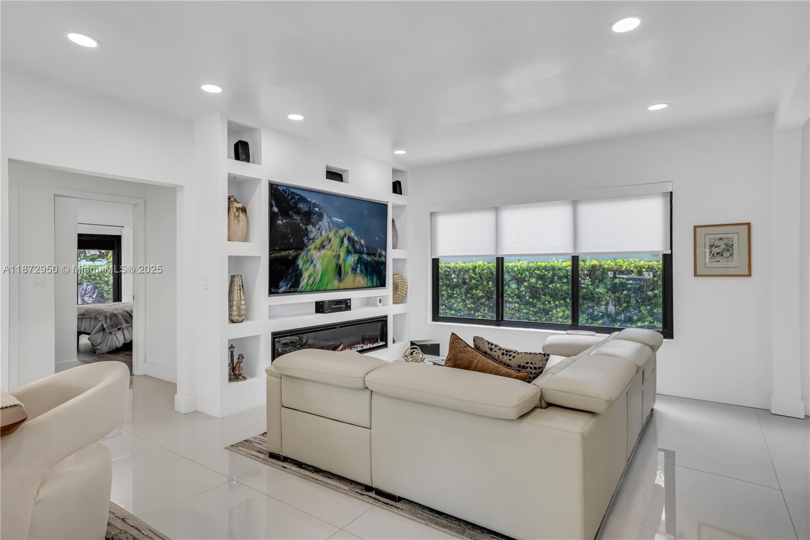 A modern living room features a white sectional sofa, built-in shelving, and a wall-mounted television — 2484 SW 25th St, Miami FL 33133, MIAMI, FL