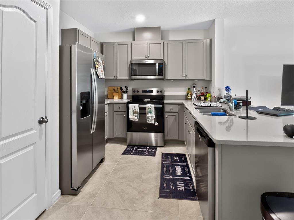 A kitchen features gray cabinets, stainless steel appliances, and a quartz-topped island with a sink — 3156 GOOSE ROAD, DAVENPORT, FL