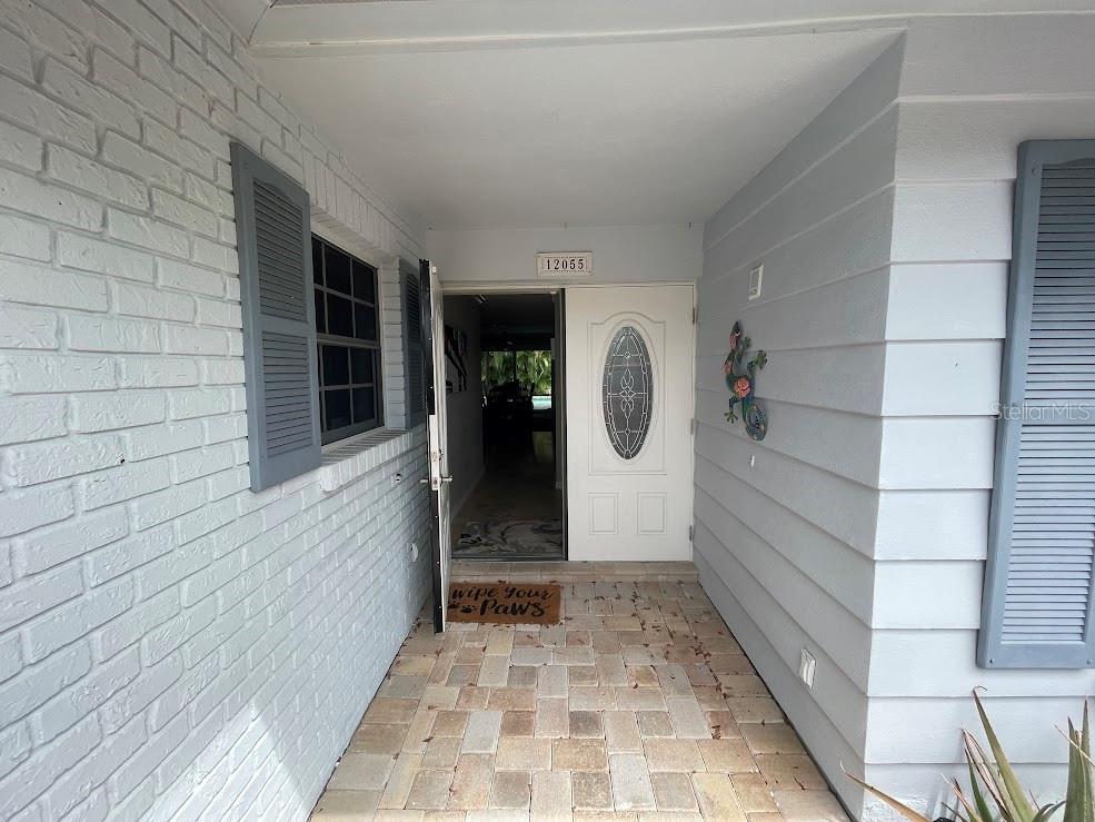 A paved entryway leads to a white front door with a decorative oval glass insert — 12055 4TH STREET E, TREASURE ISLAND, FL