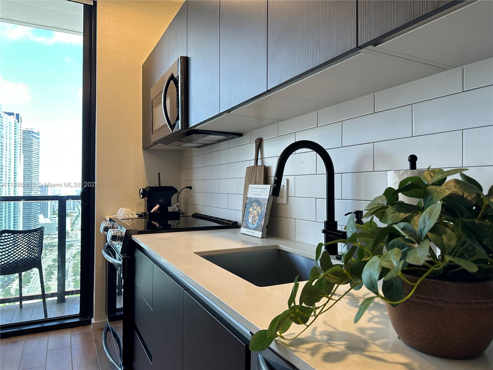 A modern kitchen features dark cabinetry, white subway tile backsplash, and a view of skyscrapers — 398 NE 5th St # 3008, Miami FL 33132, MIAMI, FL