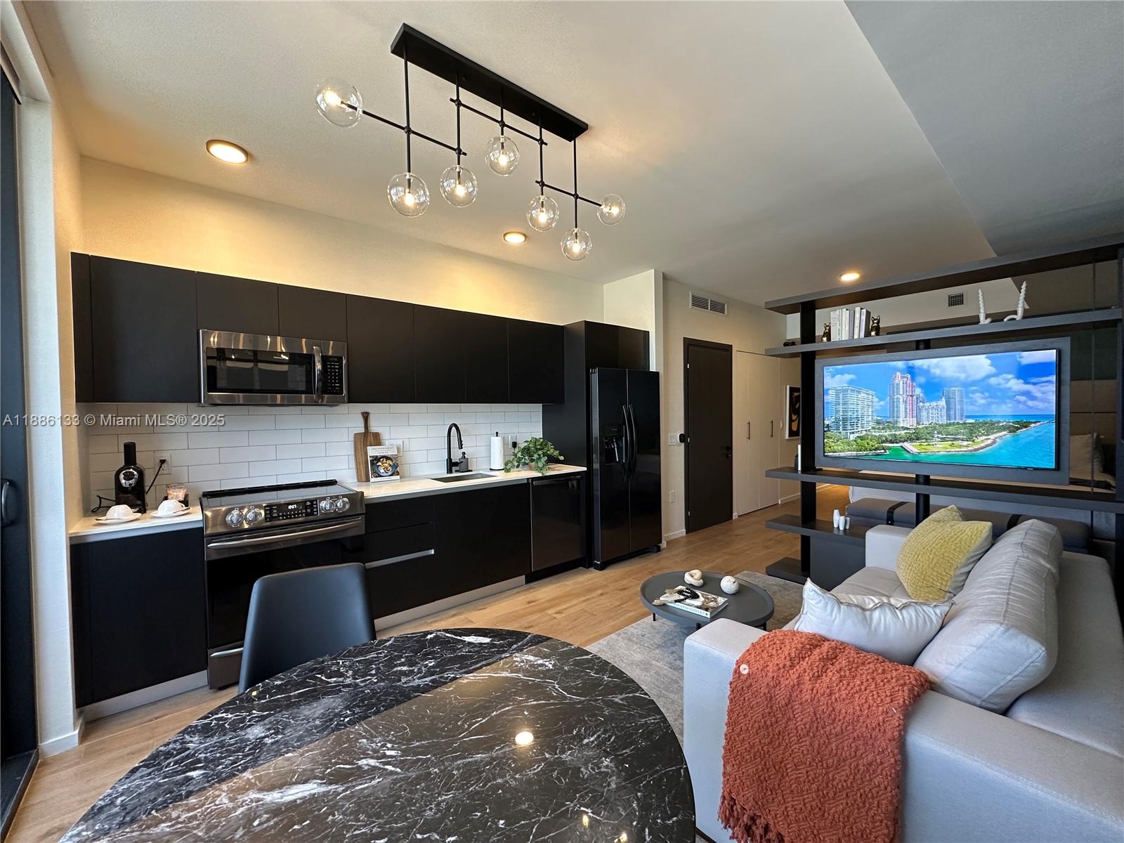 A modern kitchen with black cabinetry and a living area featuring a television room divider — 398 NE 5th St # 3008, Miami FL 33132, MIAMI, FL