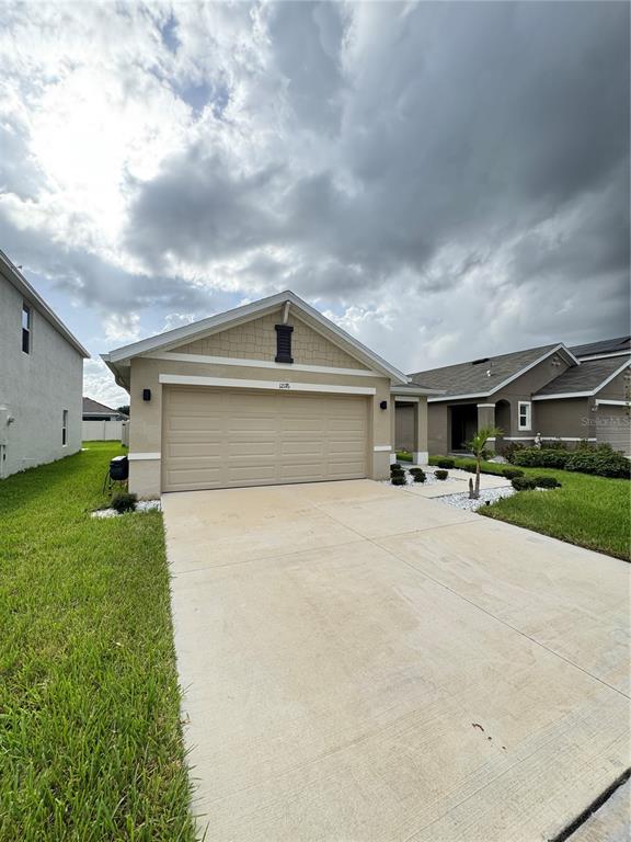 A tan single-story house with a two-car garage and a concrete driveway under cloudy skies — 12176 WATER ASH PLACE, RIVERVIEW, FL