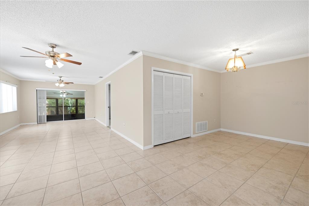 A living area with beige tile floors, white louvered closet doors, and multiple ceiling fans — 3820 LIGHTHOUSE WAY, NEW PORT RICHEY, FL