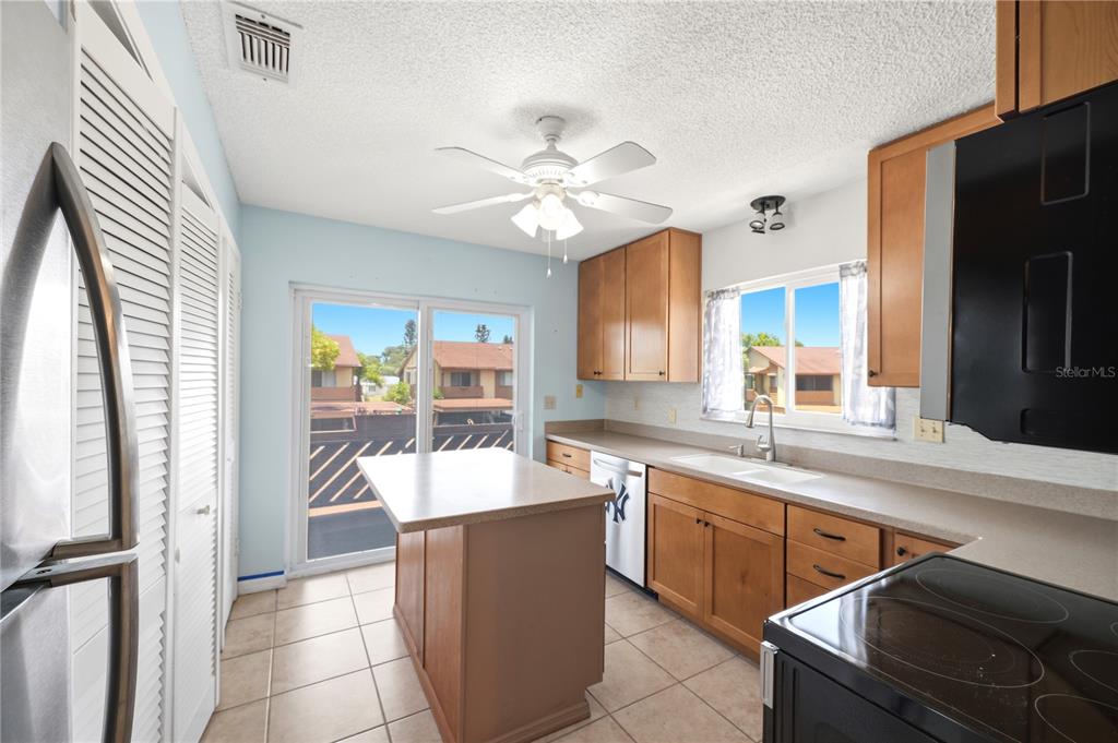 A kitchen with light wood cabinets, a central island, tile flooring, and a sliding glass door — 3820 LIGHTHOUSE WAY, NEW PORT RICHEY, FL