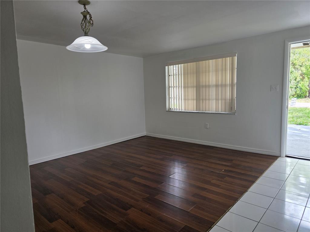 An empty room features dark wood-look flooring, white walls, a pendant light, and vertical blinds — 1212 E CHILKOOT AVENUE, TAMPA, FL