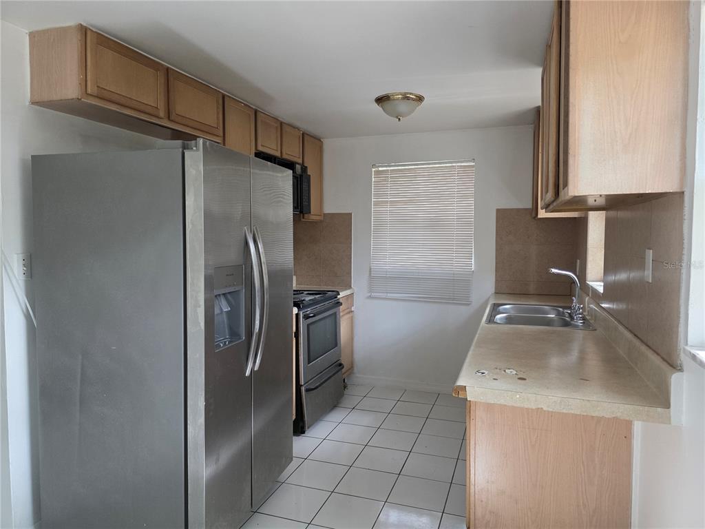 A kitchen features stainless steel appliances, light wood cabinets, tiled floors, and a double sink — 1212 E CHILKOOT AVENUE, TAMPA, FL