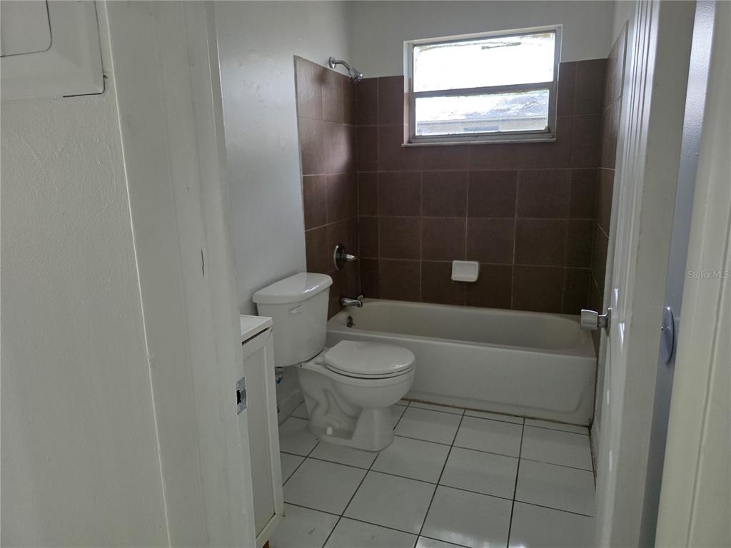 A bathroom features a white toilet, a white bathtub with brown tile walls, and white flooring — 1212 E CHILKOOT AVENUE, TAMPA, FL