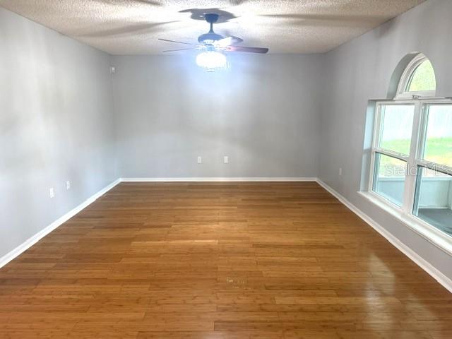 An empty room with light gray walls, bamboo flooring, a ceiling fan, and arched windows — 409 YEARLING COVE LOOP, APOPKA, FL