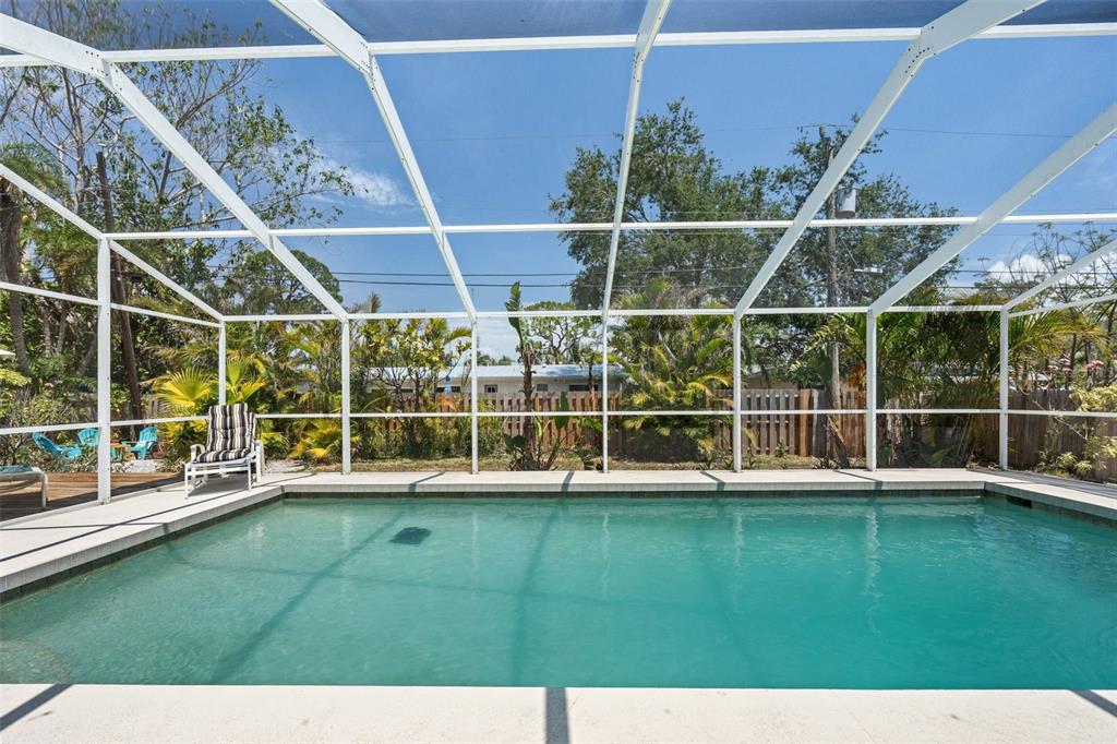 A swimming pool enclosed by a white screen cage in a backyard with tropical landscaping — 139 ADAIR AVENUE, SARASOTA, FL