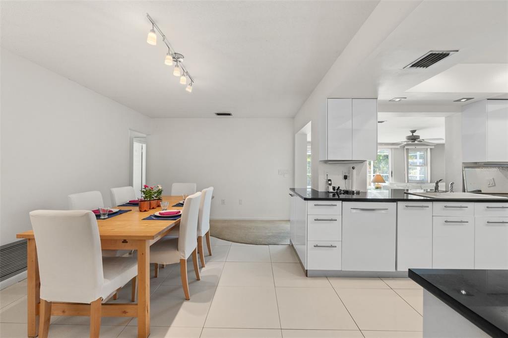 A dining area with a wooden table and white chairs sits beside a modern white kitchen — 139 ADAIR AVENUE, SARASOTA, FL