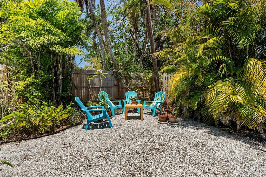 A gravel patio features four turquoise chairs and a small wooden table near a fence — 139 ADAIR AVENUE, SARASOTA, FL