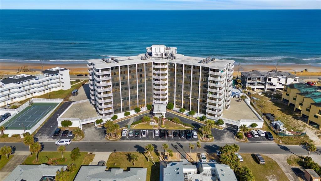 An aerial view shows a multi-story beachfront condominium building with a parking lot and tennis court — 3580 S OCEAN SHORE BOULEVARD UNIT 204, FLAGLER BEACH, FL