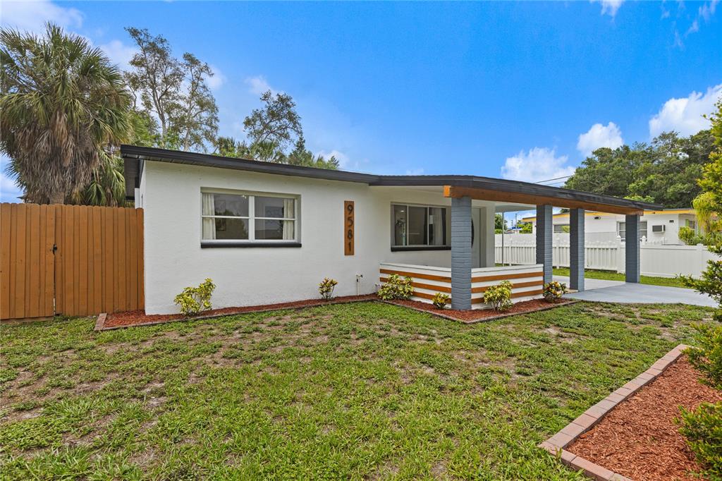 A white, single-story house with a flat roof, a covered porch, and a wooden fence — 9581 49TH WAY N, PINELLAS PARK, FL