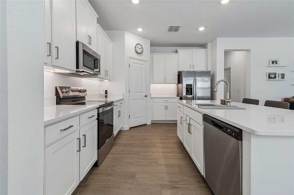 A modern kitchen features white cabinets, stainless steel appliances, a large island, and wood-look flooring — 31735 GRIFFIN SANDS LANE, SAN ANTONIO, FL