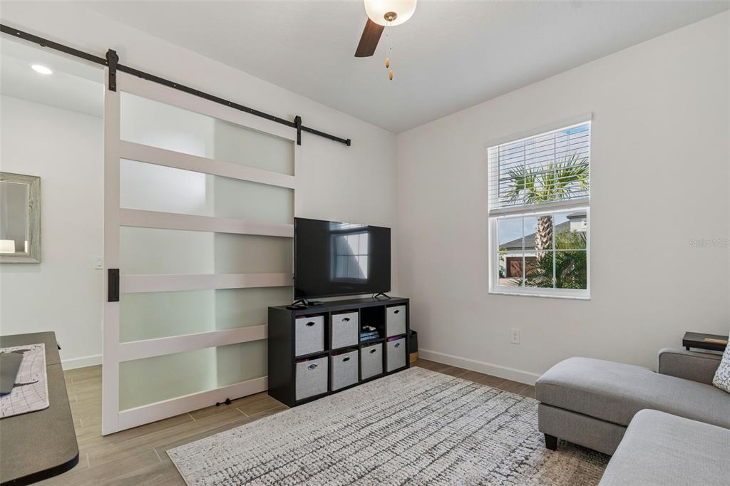 A room features a sliding frosted glass barn door, a television on a storage unit, and a window — 31735 GRIFFIN SANDS LANE, SAN ANTONIO, FL