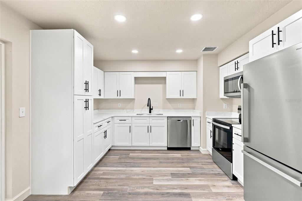 A kitchen with white cabinets, stainless steel appliances, and wood-look flooring — 6204 ASHLAND AVENUE, LEESBURG, FL