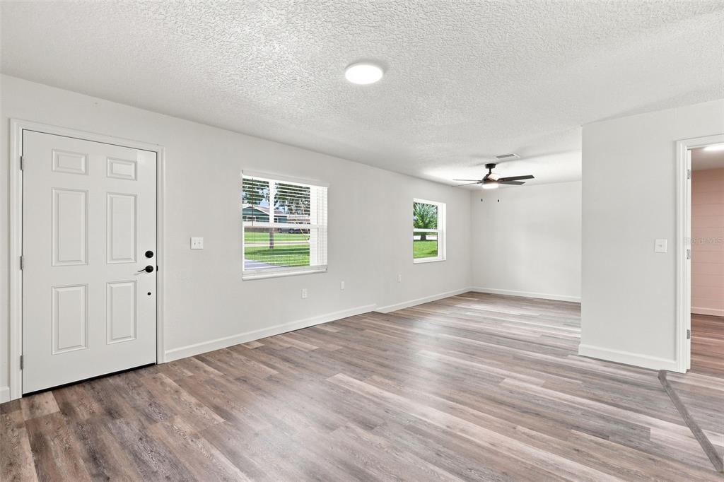 A bright living room features light gray walls, wood-look flooring, and a ceiling fan — 6204 ASHLAND AVENUE, LEESBURG, FL