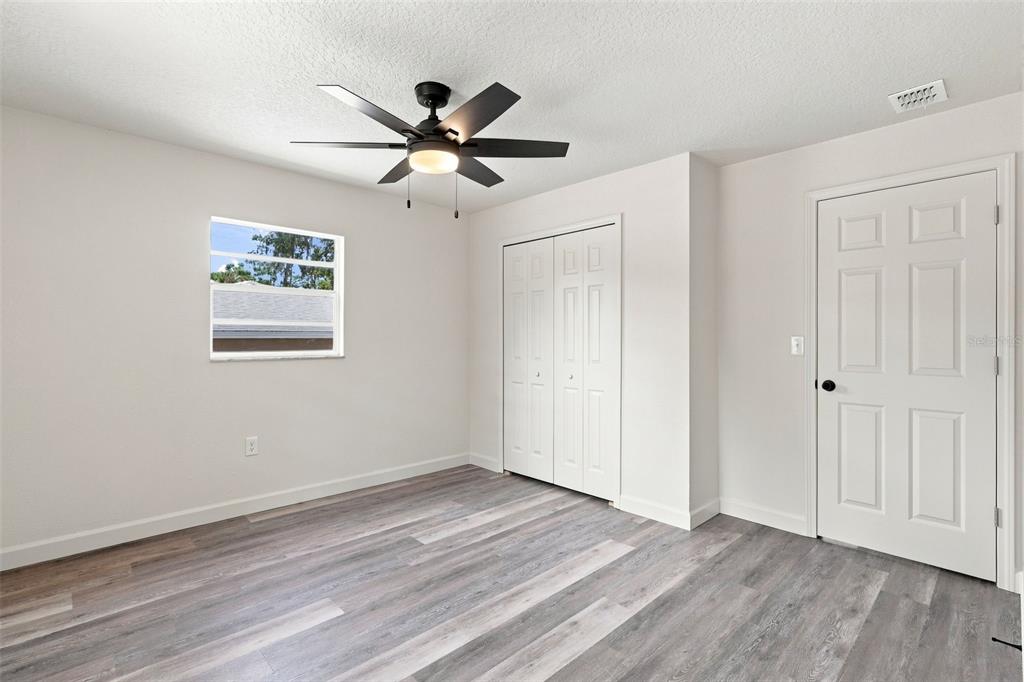 A bedroom with light walls, gray wood-look flooring, a ceiling fan, and a white door — 6204 ASHLAND AVENUE, LEESBURG, FL